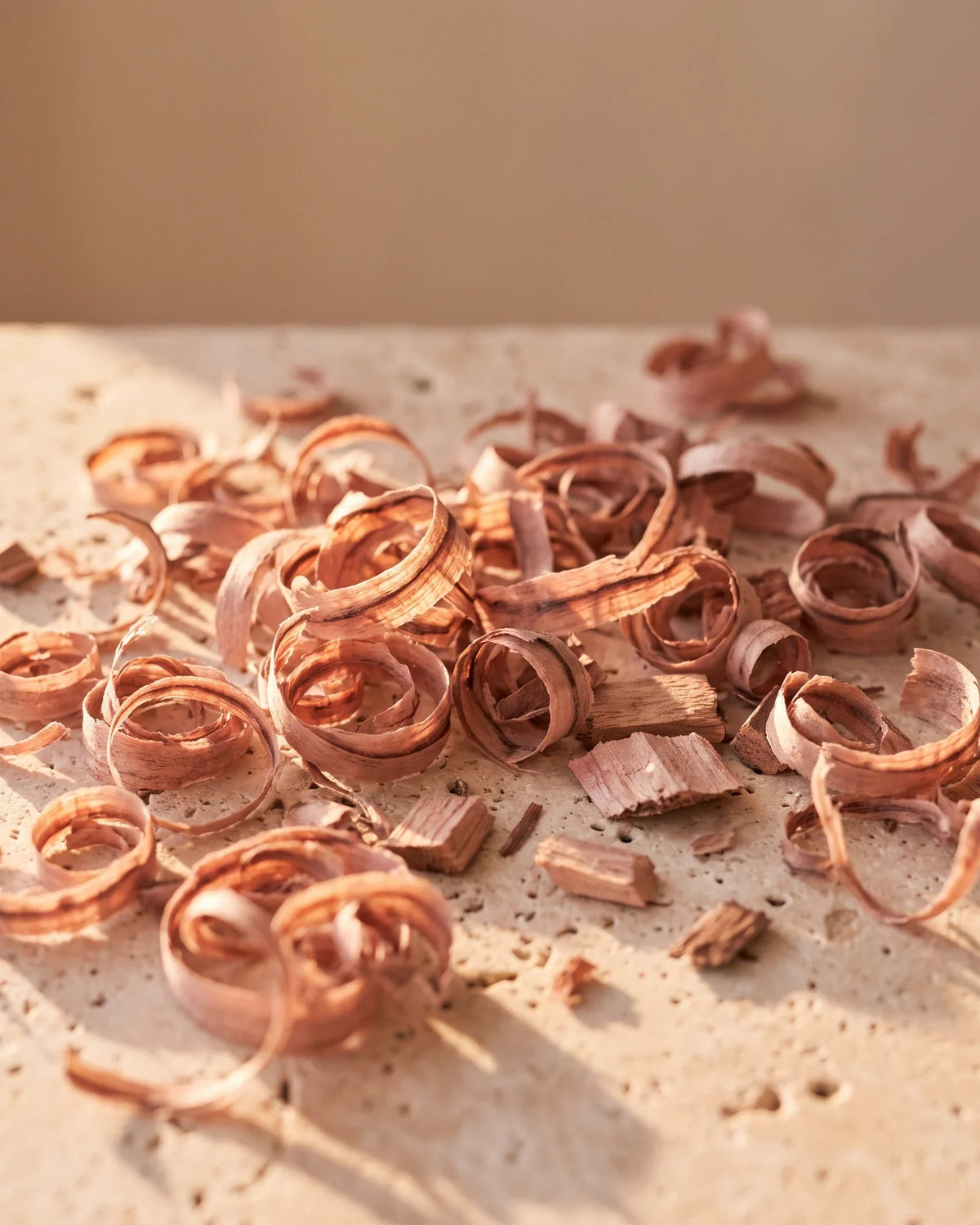 Fine rosy rosewood shavings glowing in warm light on travertine — the sweet, floral-woody scent of Delune Brazilian Rosewood Pure Essential Oil