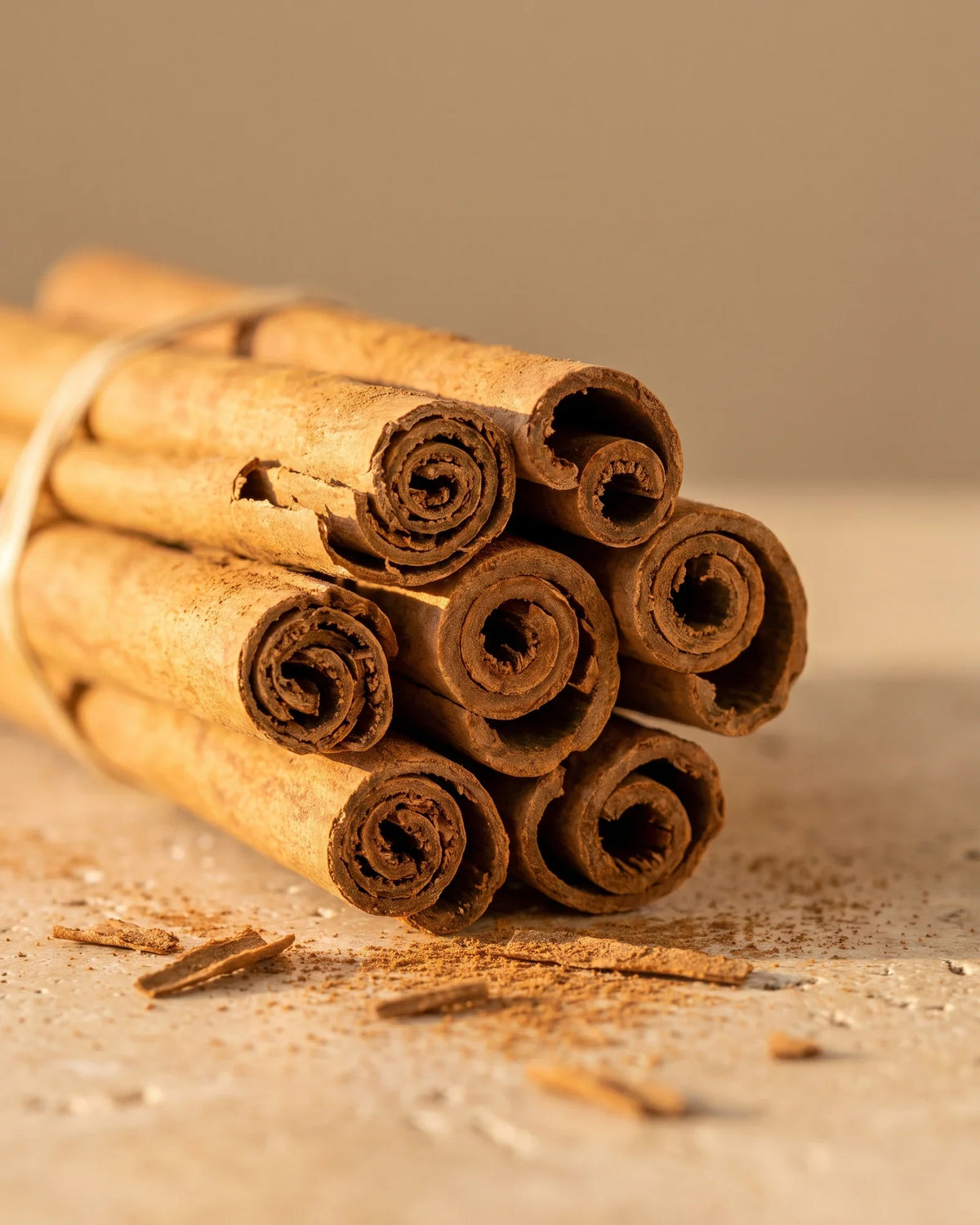 A bundle of cinnamon quills with a dusting of ground cinnamon on travertine — the sweet, warm spice scent of Delune Cinnamon Pure Essential Oil
