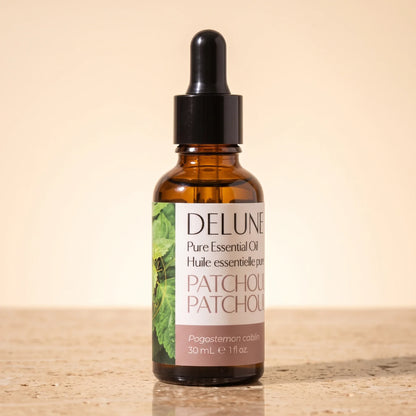 Delune Patchouli Pure Essential Oil, 30ml amber glass dropper bottle on warm travertine stone