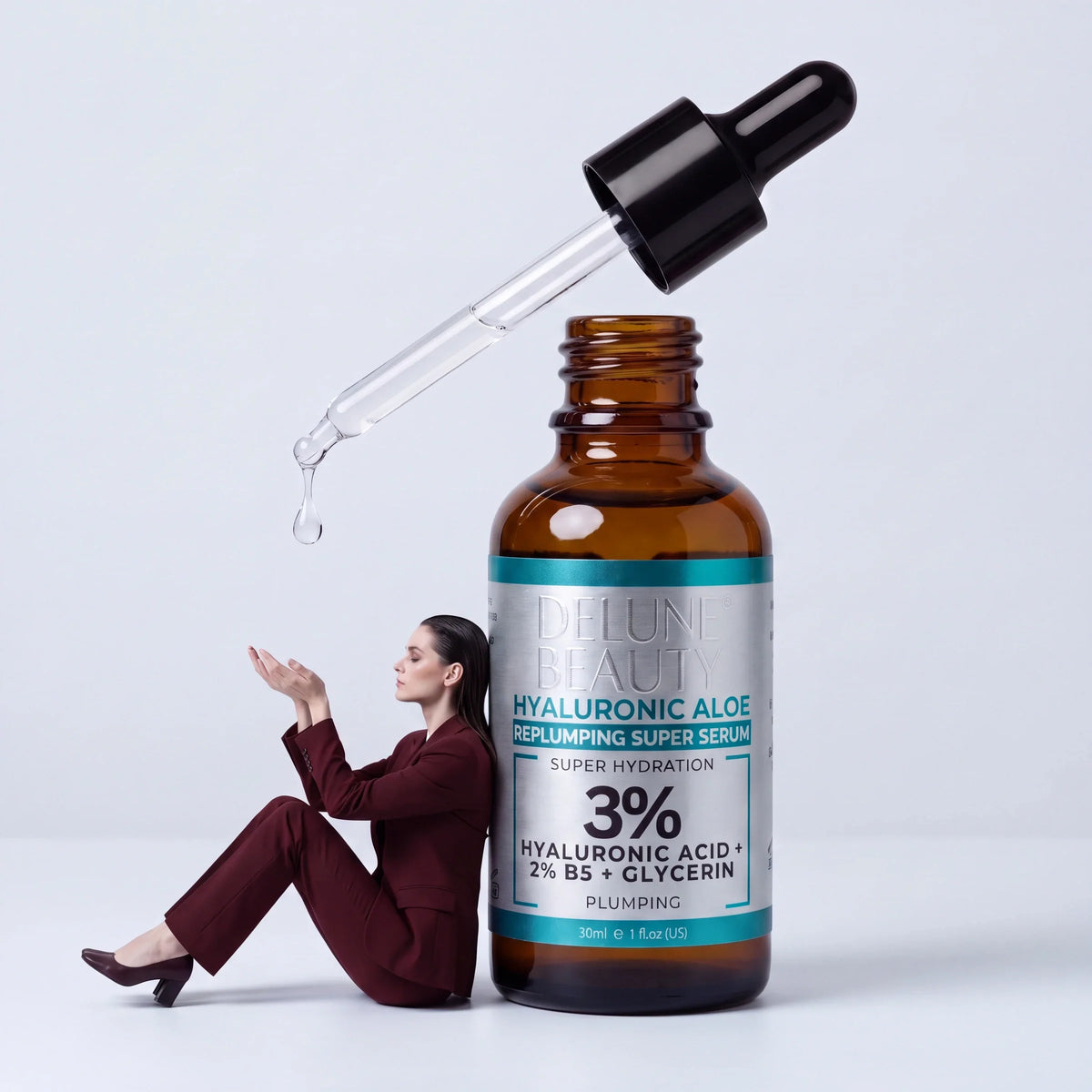 Restore: a woman in an oxblood suit leans against a giant Delune Hyaluronic Aloe serum, catching a falling drop